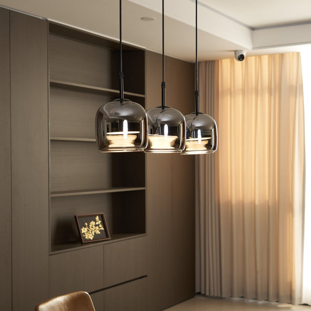 Clérachic smoke gray pendants hung as a trio beside a built-in shelf, daylight from the curtain catching the mirrored domes.