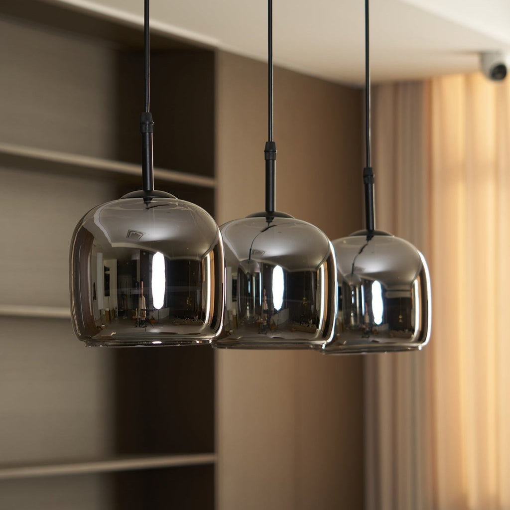 Close angled view of three Clérachic smoke gray domes, their mirrored surfaces reflecting the room while warm light sits underneath.