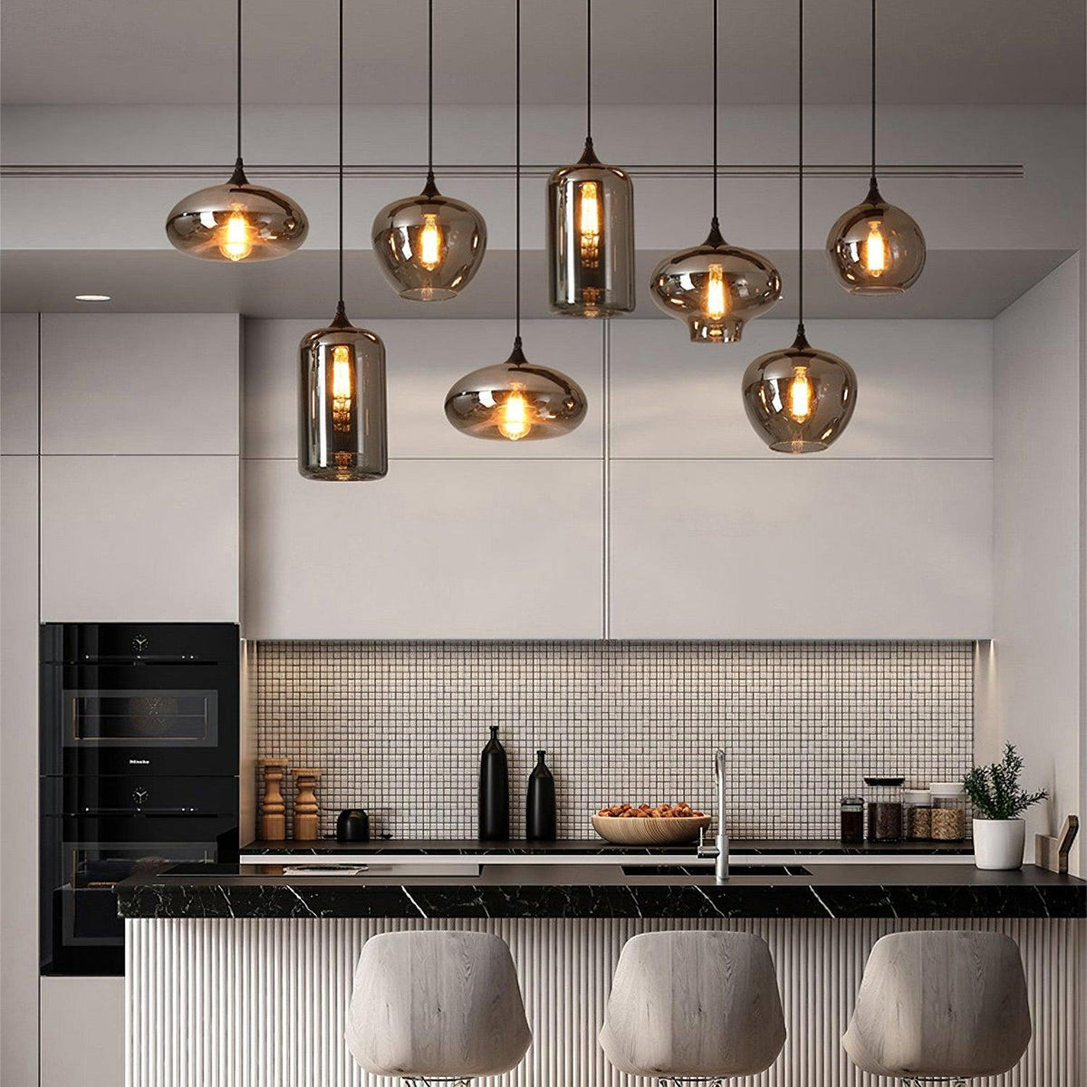 The same Clérachic pendant seen again in a white kitchen, its smoke glass shades lit above a black marble worktop.