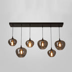 Six smoke glass globes hang from a long black canopy on this Clérachic pendant, shown lit on a pale grey backdrop.