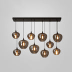 Ten glass shades on a black rectangular canopy, part of this Clérachic pendant, glow warm on a plain grey backdrop.