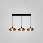 Three flattened smoke glass shades hang evenly from a slim black canopy on this Clérachic pendant, lit warm on grey.