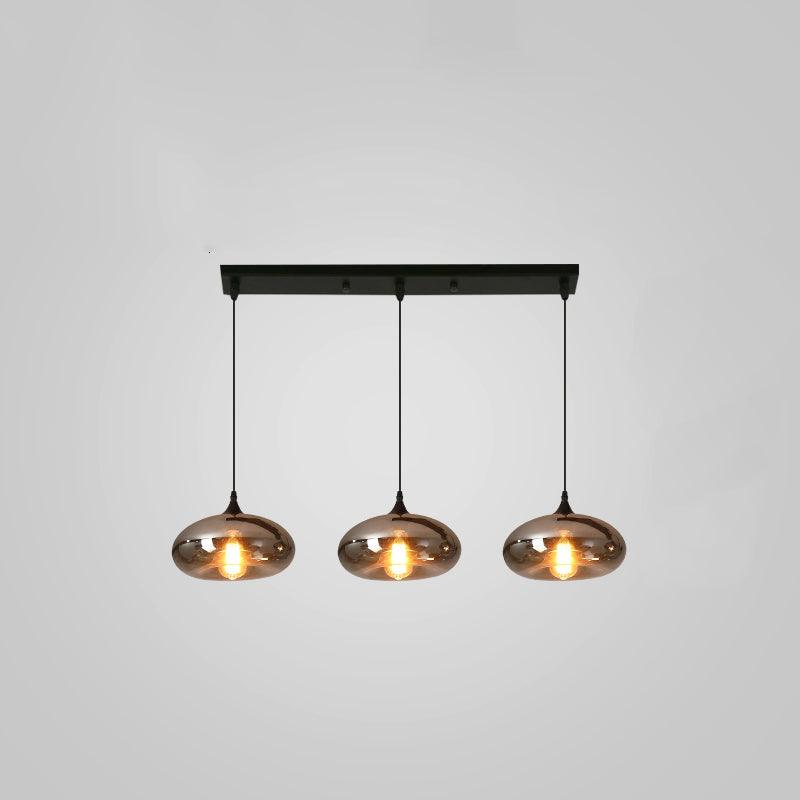 Three flattened smoke glass shades hang evenly from a slim black canopy on this Clérachic pendant, lit warm on grey.