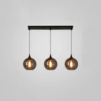Three round smoke glass globes hang from a slim black canopy on this Clérachic pendant, lit against a grey backdrop.
