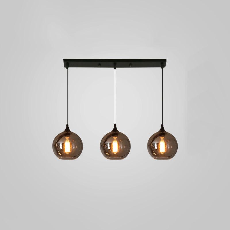 Three round smoke glass globes hang from a slim black canopy on this Clérachic pendant, lit against a grey backdrop.