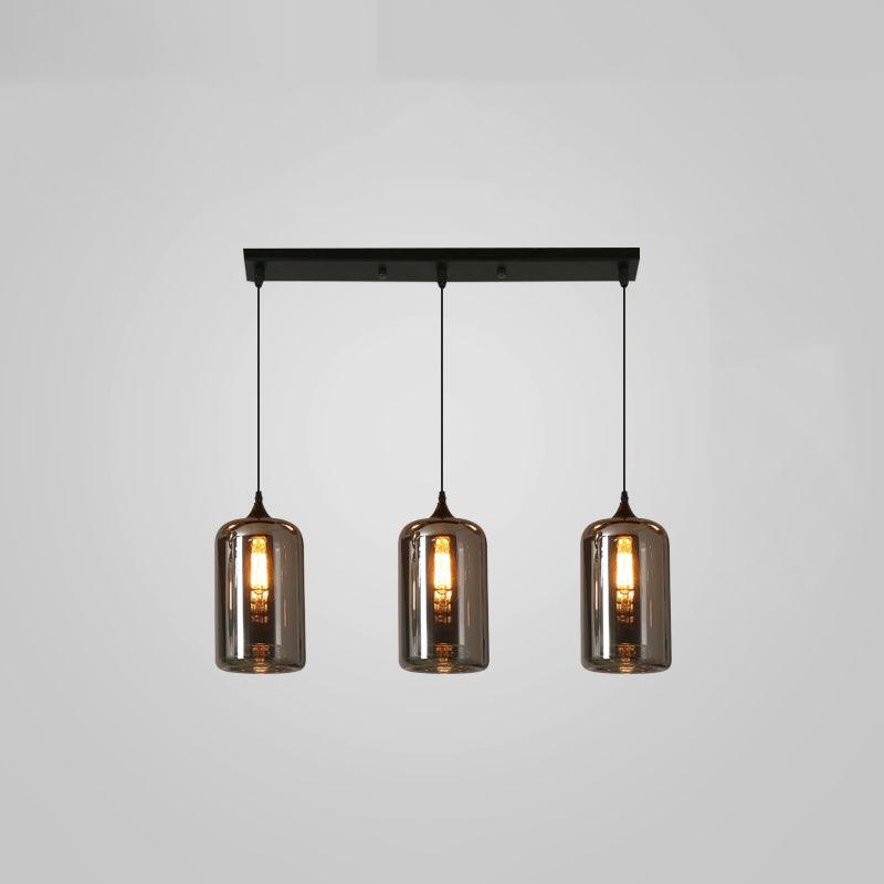 Three tall smoke glass cylinders hang in a row from a slim black canopy on this Clérachic pendant, filament bulbs lit.