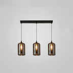 Three tall smoke glass cylinders hang in a row from a slim black canopy on this Clérachic pendant, filament bulbs lit.