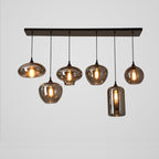 Six mixed shades on this Clérachic pendant hang below a black canopy: flat discs, globes and one tall cylinder, lit warm.