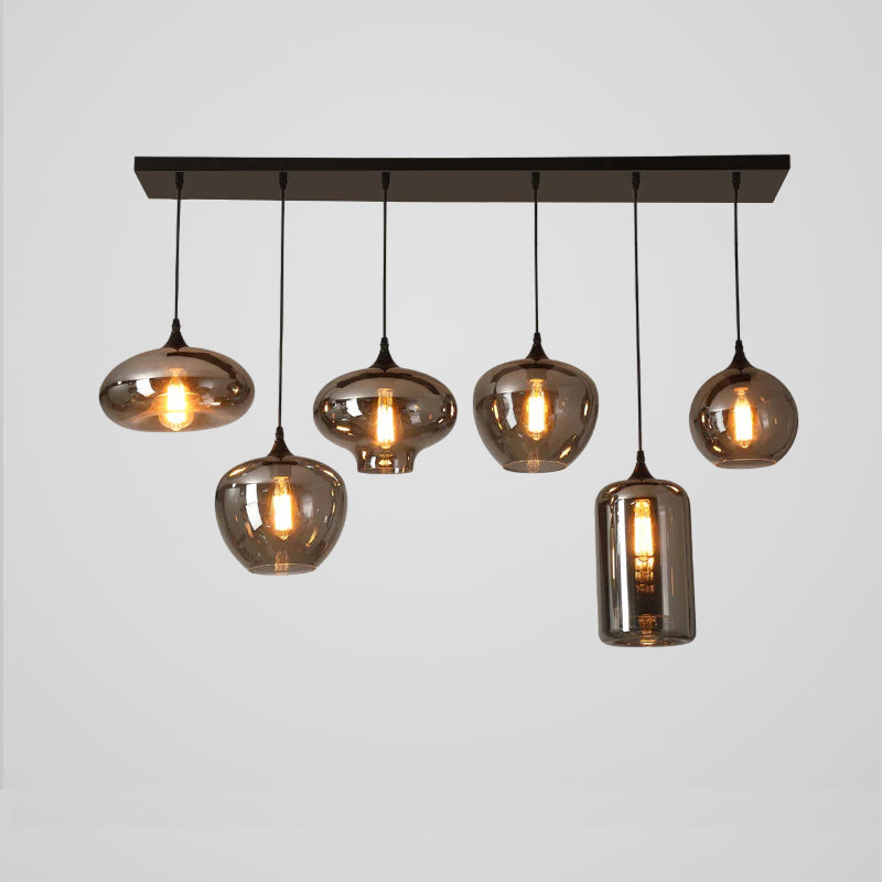 Six mixed shades on this Clérachic pendant hang below a black canopy: flat discs, globes and one tall cylinder, lit warm.