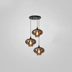 Three narrow-necked smoke glass shades hang from a round black canopy on this Clérachic pendant, glowing warm.