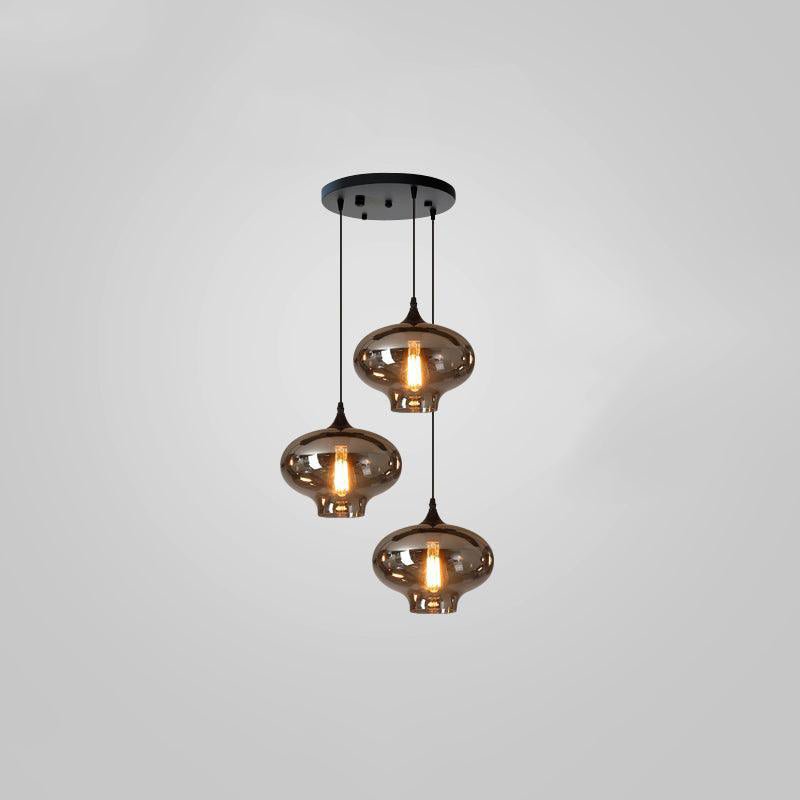 Three narrow-necked smoke glass shades hang from a round black canopy on this Clérachic pendant, glowing warm.
