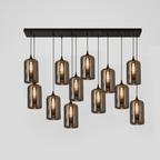 Twelve smoke glass cylinders hang from a long black canopy on this Clérachic pendant, each with a lit filament bulb.