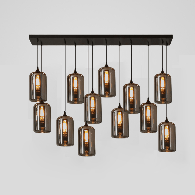 Twelve smoke glass cylinders hang from a long black canopy on this Clérachic pendant, each with a lit filament bulb.