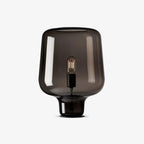 This Clérachic table lamp on a plain white backdrop, a smoke grey glass shade with a visible filament bulb on a small black base.