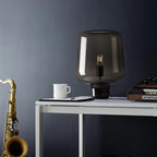 Against a navy wall, this Clérachic glass table lamp stands on a white desk beside a mug, a synthesiser and a saxophone.