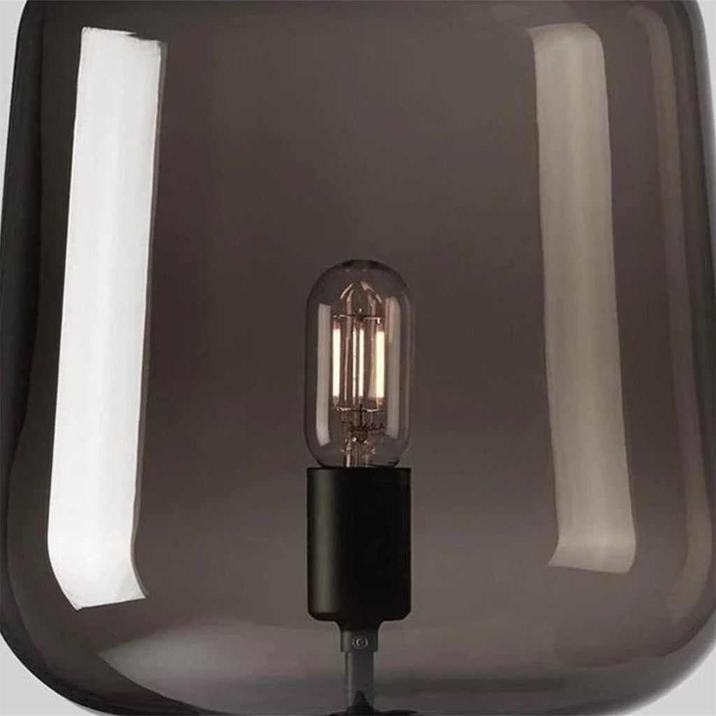 Close view of the filament bulb and black socket inside the smoke grey glass shade of this Clérachic table lamp.