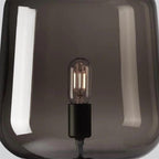 Close view of the filament bulb and black socket inside the smoke grey glass shade of this Clérachic table lamp.
