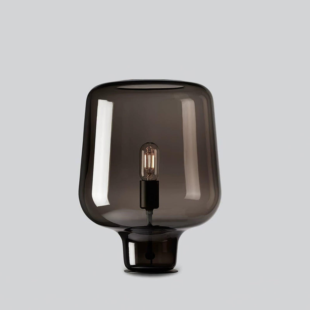 A Clérachic smoke grey glass table lamp on a light grey backdrop, its curved shade flaring over a short glass foot.