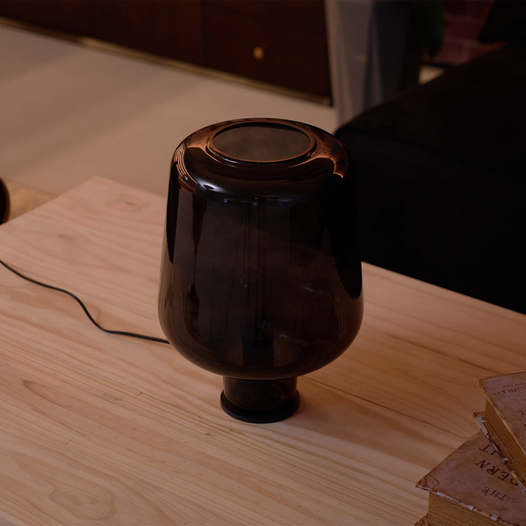Top-down angle on the open top of this Clérachic smoke grey glass table lamp, sitting on a pale wood tabletop.