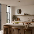 Clérachic disc pendant with smoke-grey glass hanging in a pale kitchen above a stone island with three wooden stools.