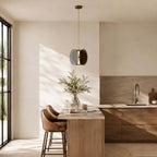 Single Clérachic glass disc pendant with a brass rod, hung in a sunlit kitchen corner beside a small breakfast bar.