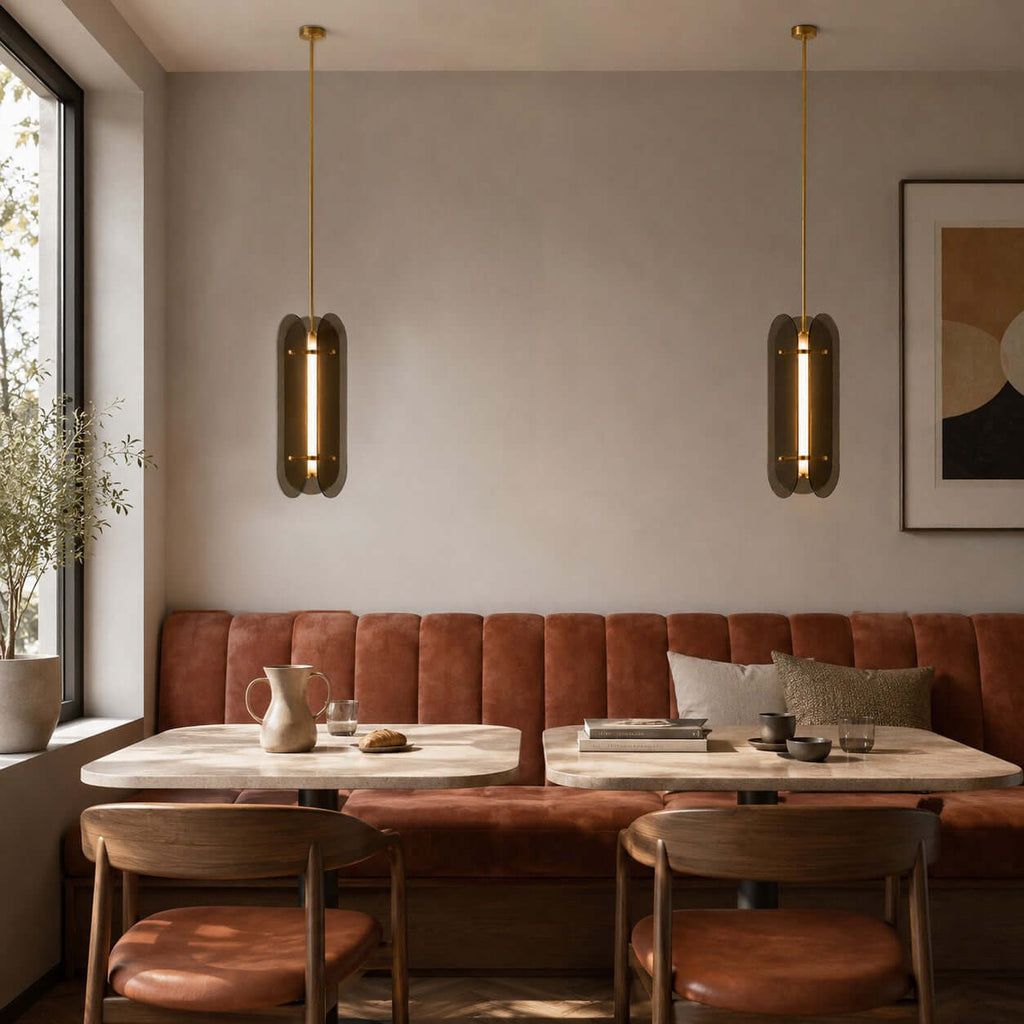 Two slim Clérachic pendants seen edge-on, their glass panels lit along the centre, above tables and a terracotta banquette.