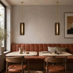 Two slim Clérachic pendants seen edge-on, their glass panels lit along the centre, above tables and a terracotta banquette.