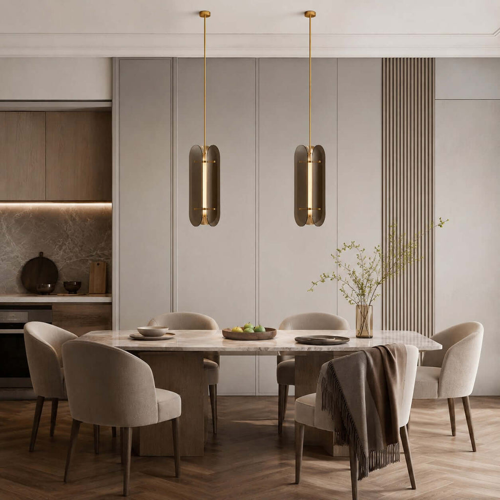 Pair of narrow Clérachic glass pendants over a long dining table with beige chairs, against a panelled grey wall.