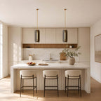 Two Clérachic column pendants in smoked glass hang above a white stone island with three cushioned stools.