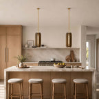 Clérachic glass pendants with brass rods hanging over a marble-topped kitchen island with four round-seated stools.