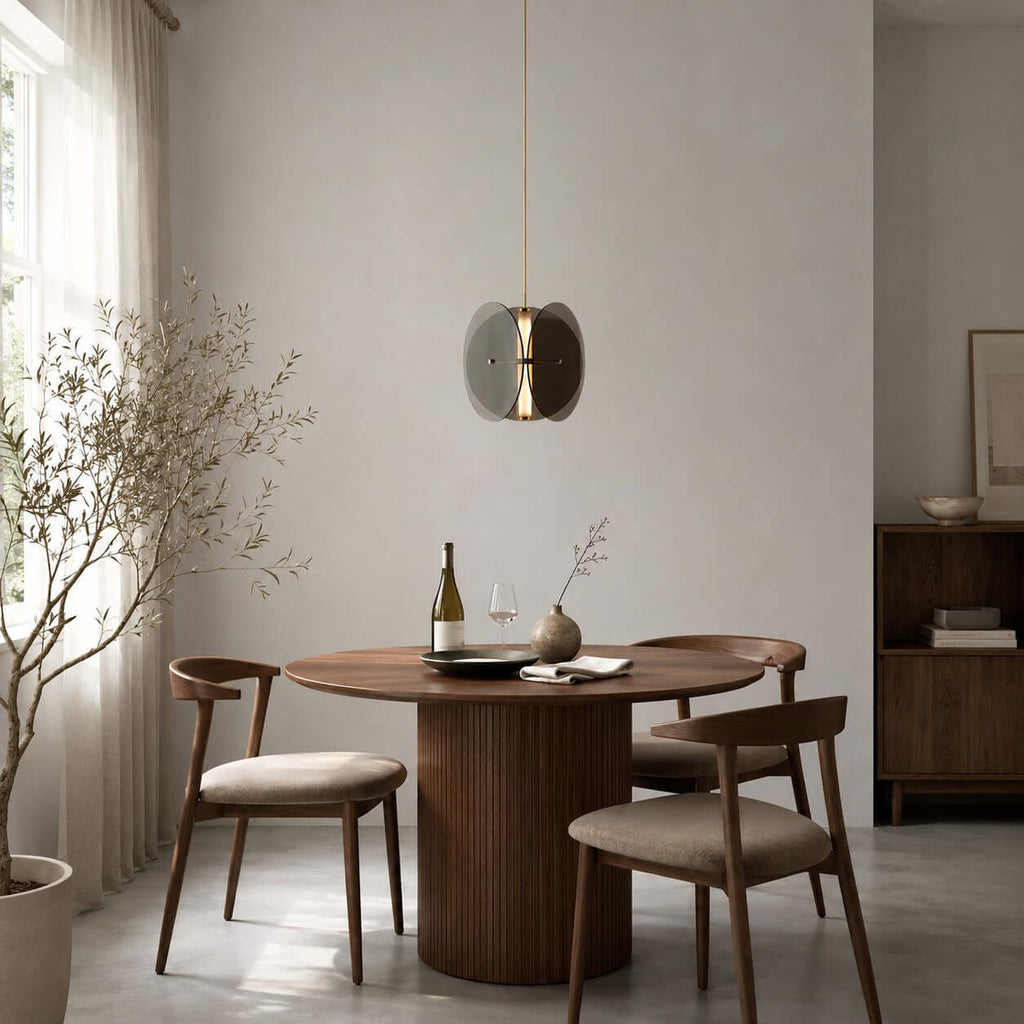 A single Clérachic disc pendant above a round walnut dining table with a bottle of wine and curved wooden chairs.