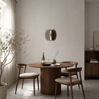 A single Clérachic disc pendant above a round walnut dining table with a bottle of wine and curved wooden chairs.