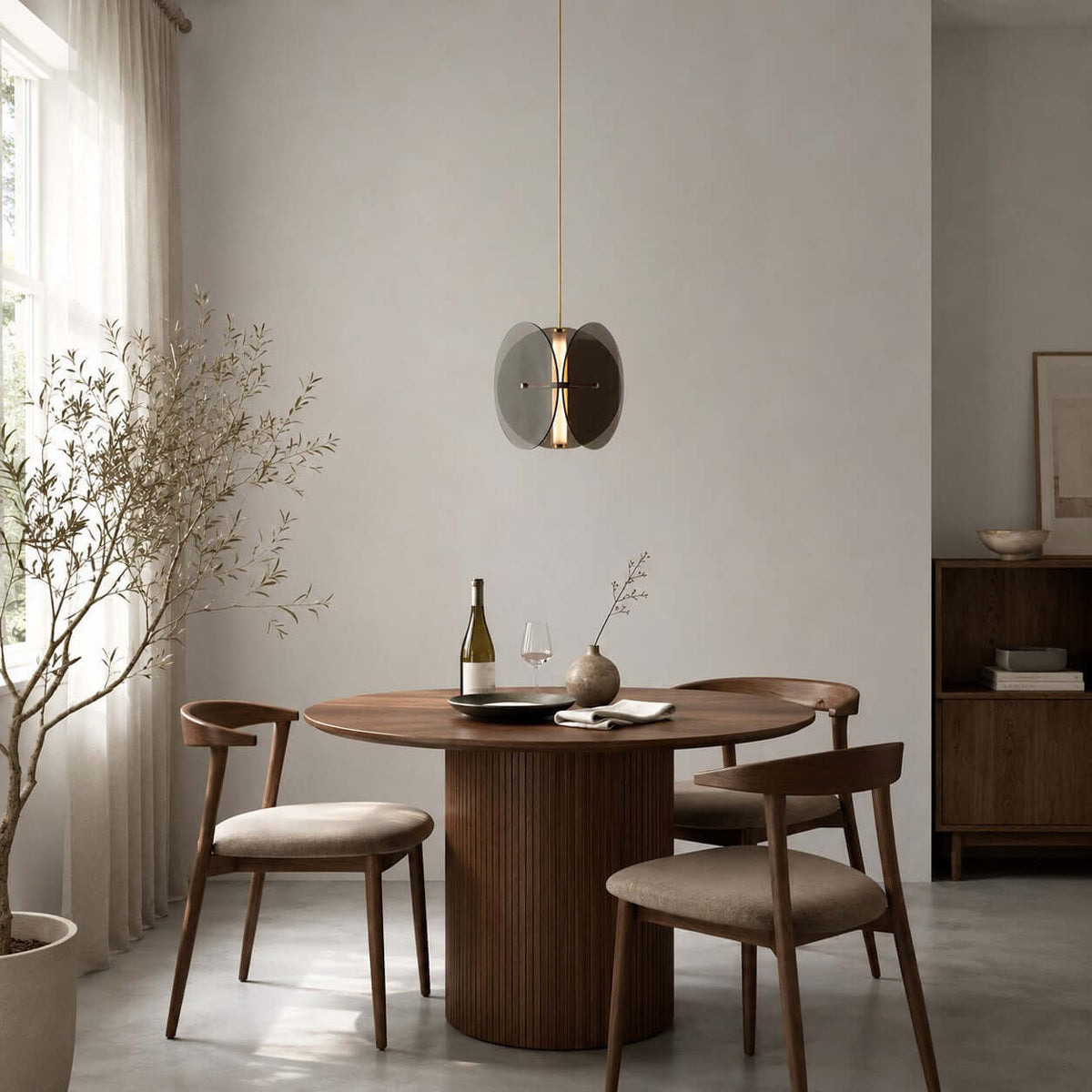 A single Clérachic disc pendant above a round walnut dining table with a bottle of wine and curved wooden chairs.