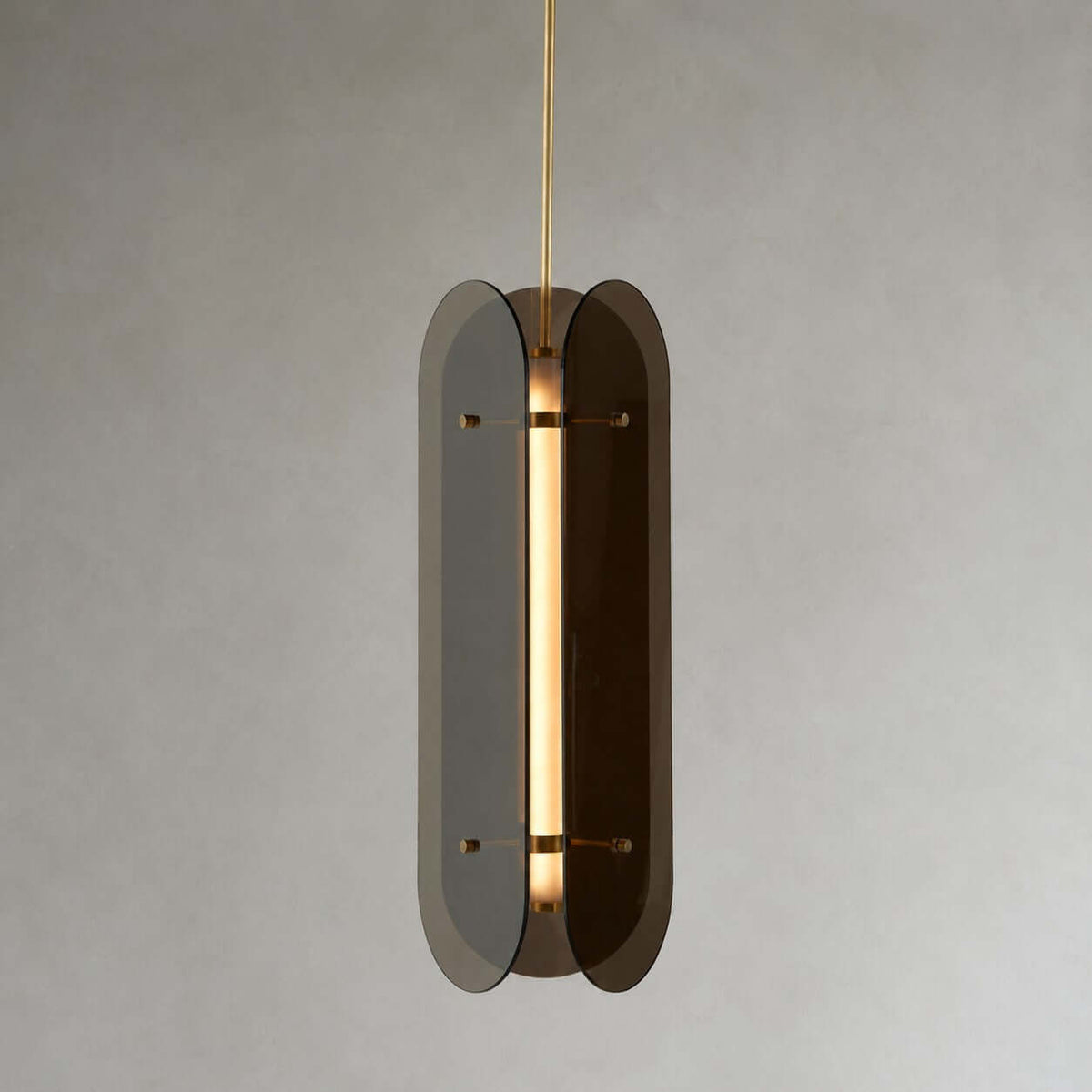 Close view of a Clérachic pendant seen edge-on, with two smoke-grey glass panels around a glowing tube on a brass rod.