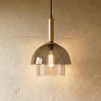 Clérachic two-tier smoked glass dome pendant on a brass stem, with a warm filament bulb lit against a textured plaster wall.
