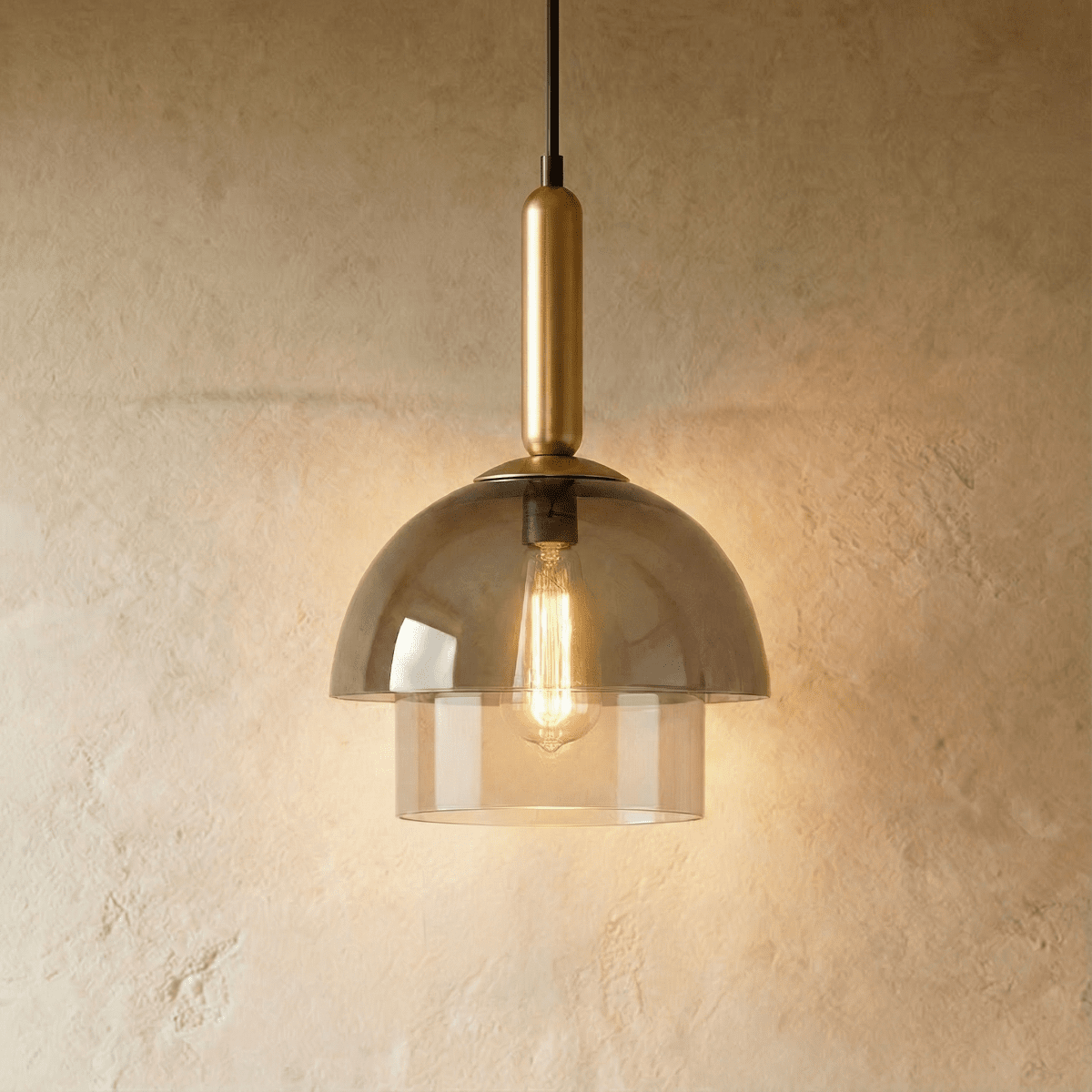 Clérachic two-tier smoked glass dome pendant on a brass stem, with a warm filament bulb lit against a textured plaster wall.