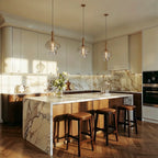Clérachic row of three smoked glass pendants with brass stems over a marble-topped kitchen island and leather-seated stools.