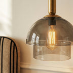Clérachic close view of a smoked glass dome and clear lower tier under a brass cap, with a warm filament bulb inside.