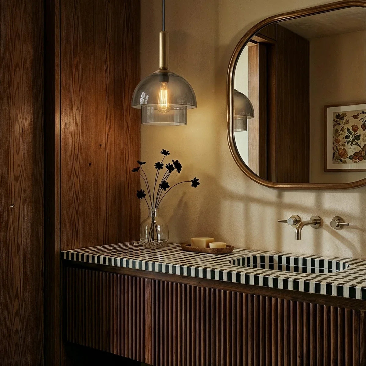 Clérachic two-tier smoked glass pendant lit above a tiled bathroom vanity, with a wooden-framed mirror and wall-mounted brass taps.
