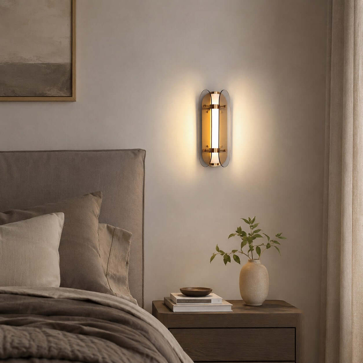 Clérachic wall light with smoked glass wings lit beside a grey upholstered headboard and a bedside table with a vase.