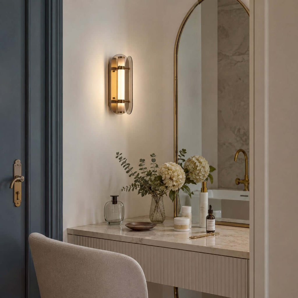 Clérachic wall sconce glowing beside an arched mirror, above a dressing table with white hydrangeas and a blue-grey door.