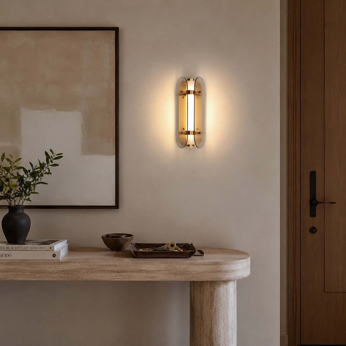 This Clérachic wall light hangs above a rounded travertine-style console with a bowl and books, beside a framed abstract artwork.