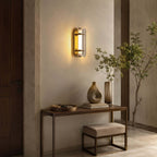 Clérachic smoked-glass wall light glowing above a console table with a vase and a stool, with a tall plant at the side.