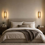 A pair of Clérachic wall lights on either side of a linen-dressed bed with a taupe throw, above matching wooden bedside tables.