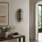 Unlit Clérachic wall light with smoked glass wings and brass details, above a dark console with a plant and a framed landscape.