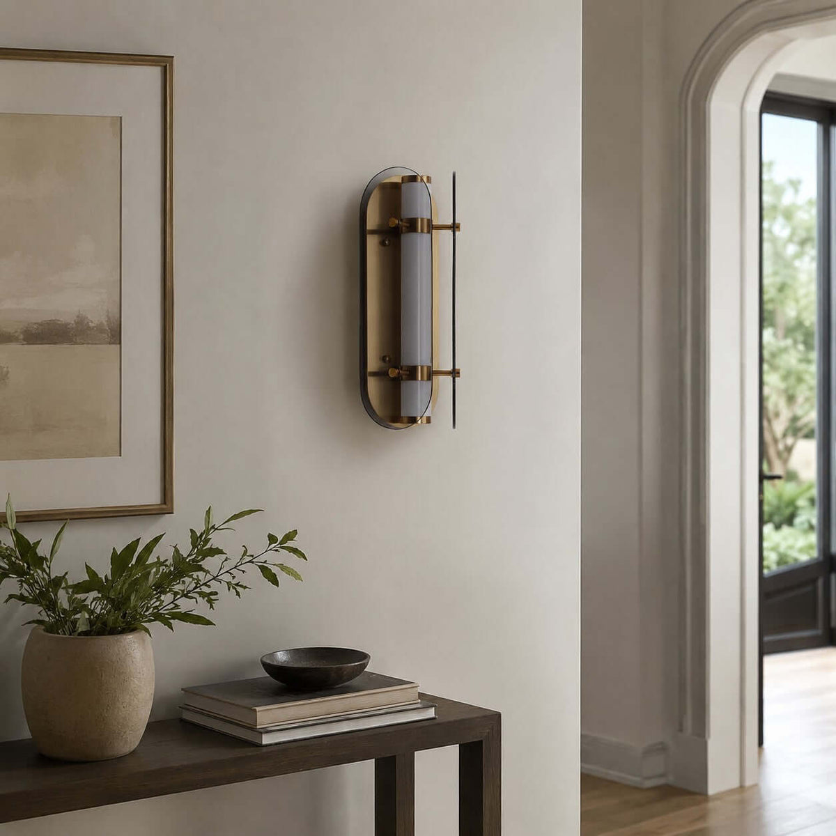 Unlit Clérachic wall light with smoked glass wings and brass details, above a dark console with a plant and a framed landscape.