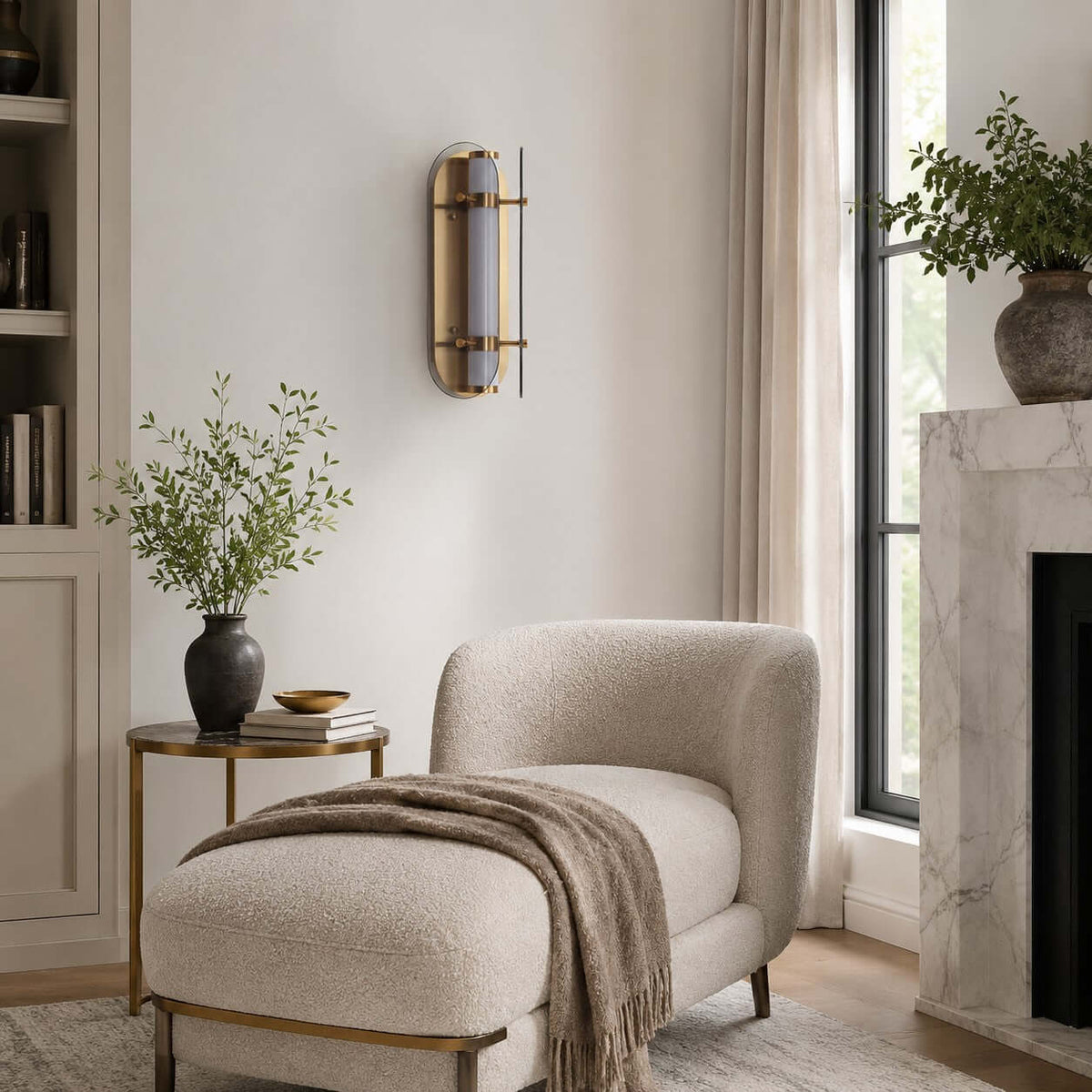 Clérachic wall light on a white wall above a boucle chaise, a marble fireplace and a tall window with a plant.