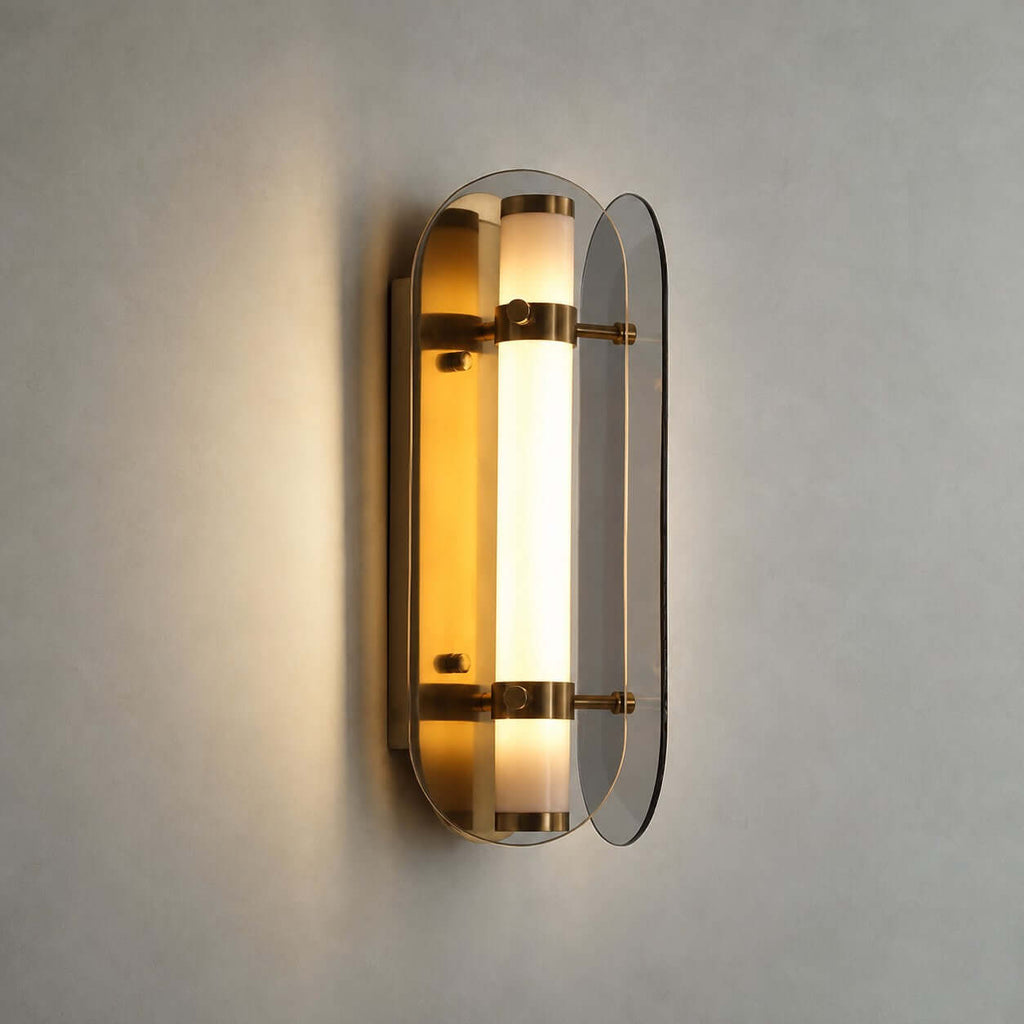 Close view of the lit Clérachic wall light, its frosted tube glowing amber between two smoked grey glass wings with brass bands.