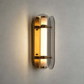 Close view of the lit Clérachic wall light, its frosted tube glowing amber between two smoked grey glass wings with brass bands.