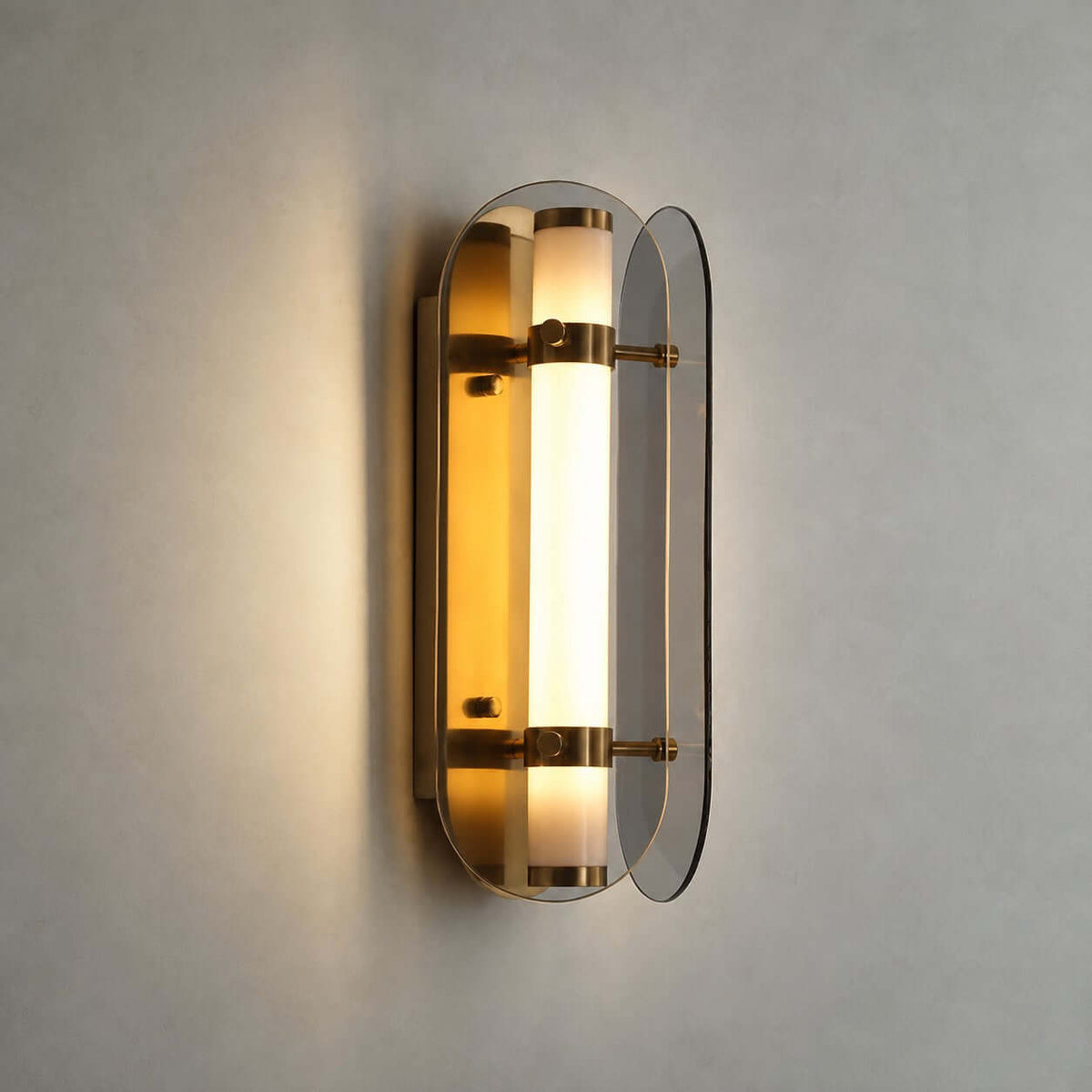 Close view of the lit Clérachic wall light, its frosted tube glowing amber between two smoked grey glass wings with brass bands.